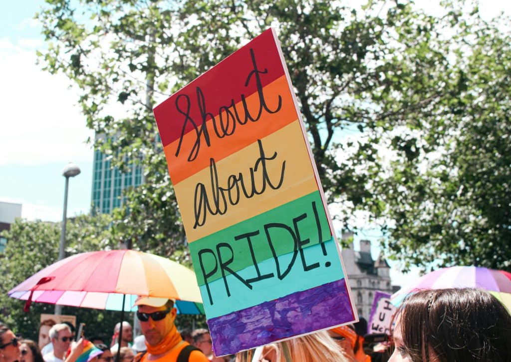 person holding sign that reads shout about pride