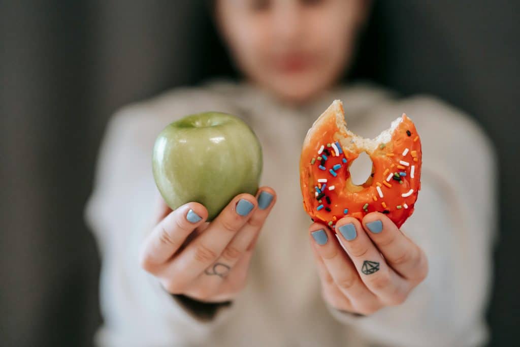hands holding up an apple and a donut