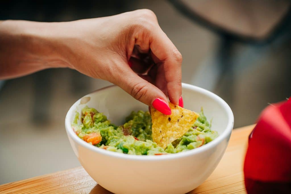 hand grabbing guacamole with chip