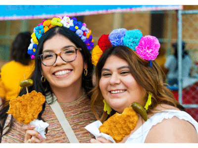 two girls smiling holding chicken on a stick