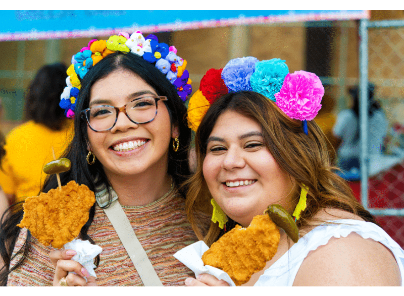 two girls smiling holding chicken on a stick