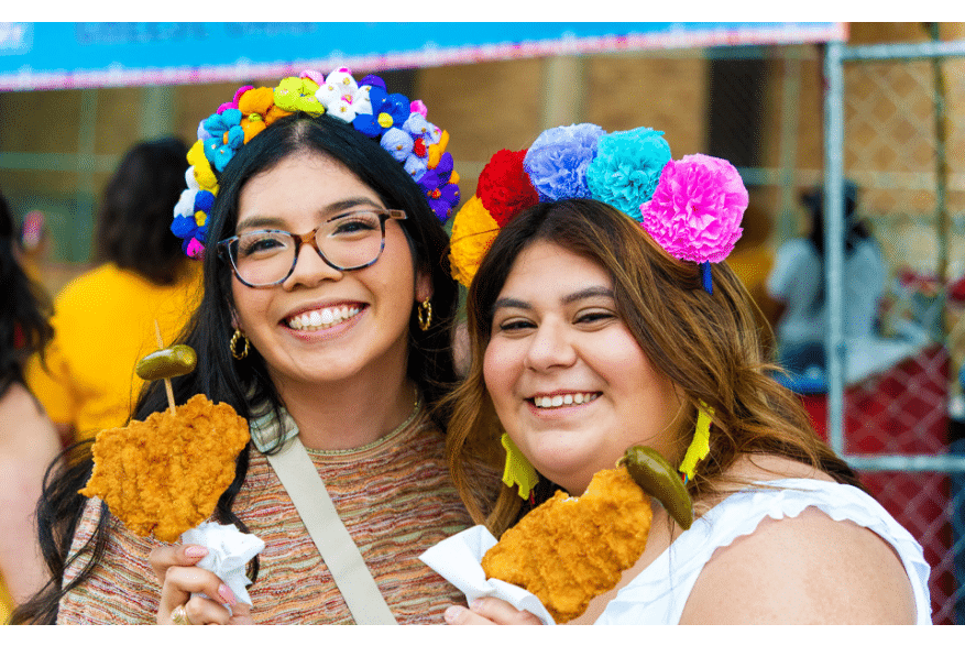 two girls smiling holding chicken on a stick