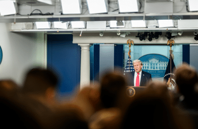 man addresses room full of journalists