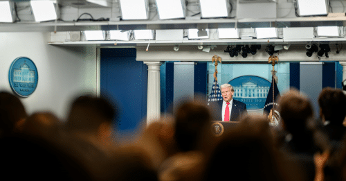 man addresses room full of journalists