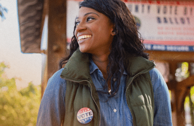 woman smiling looking to the side wearing a pin that says vote