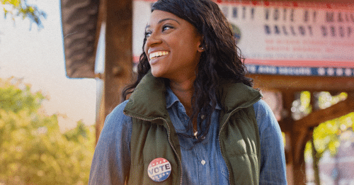 woman smiling looking to the side wearing a pin that says vote