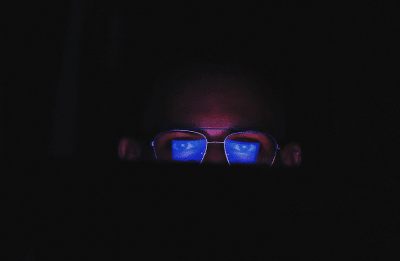 man with glasses in the dark looking at screen