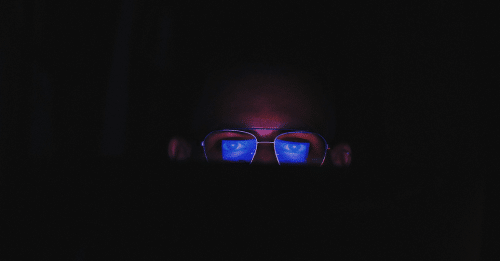 man with glasses in the dark looking at screen