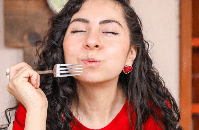 A woman in a red shirt enjoys a fresh salad indoors, capturing a moment of culinary delight