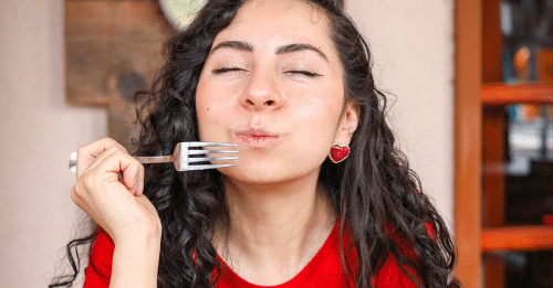 A woman in a red shirt enjoys a fresh salad indoors, capturing a moment of culinary delight