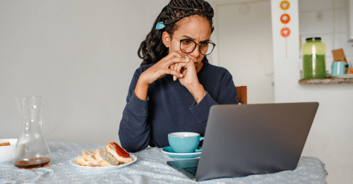 A woman concentrates while working on her laptop at home, enjoying coffee and bread